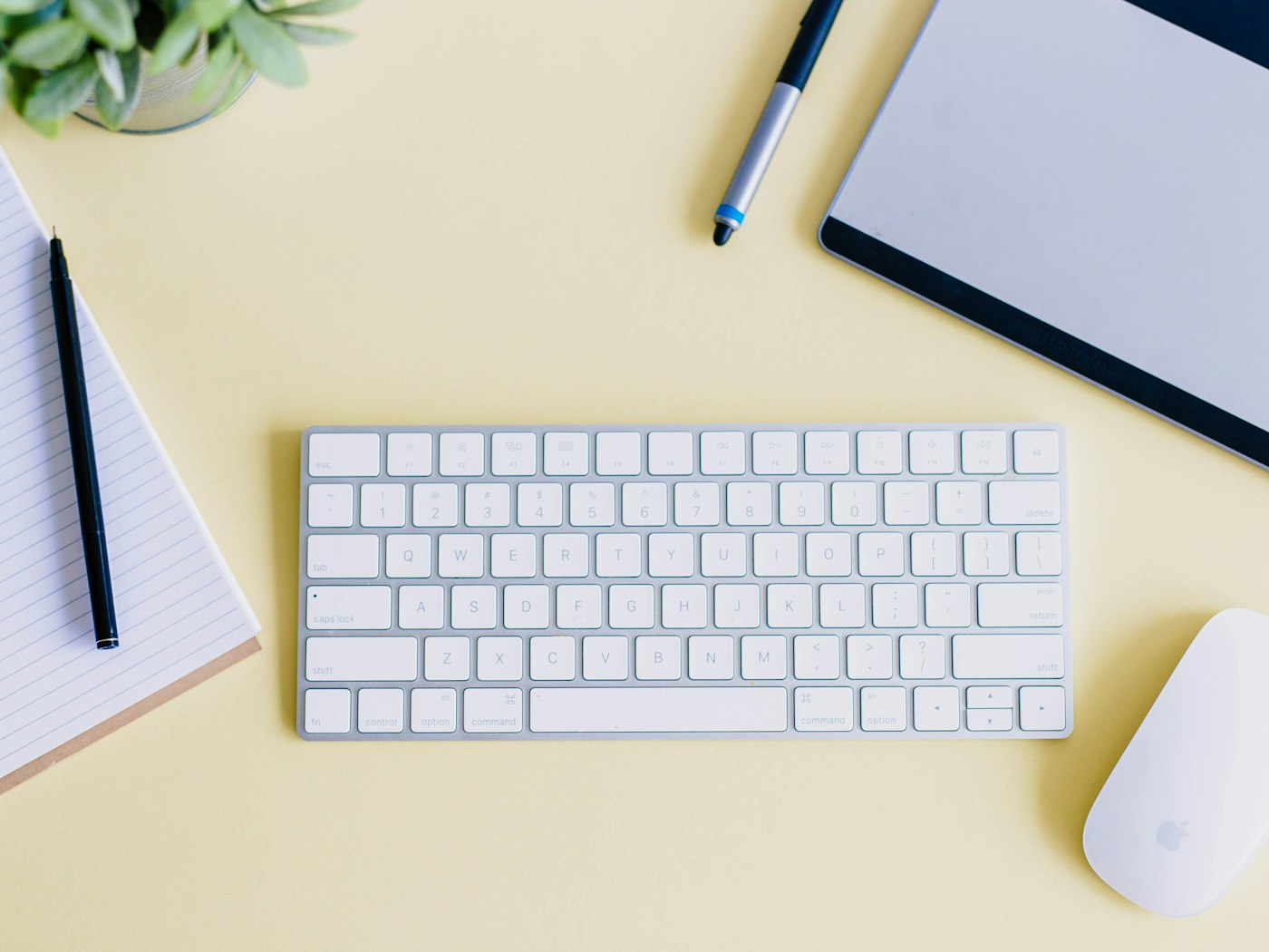 Yellow designer desk with a keyboard, notebook, pen, drawing tablet, and mouse